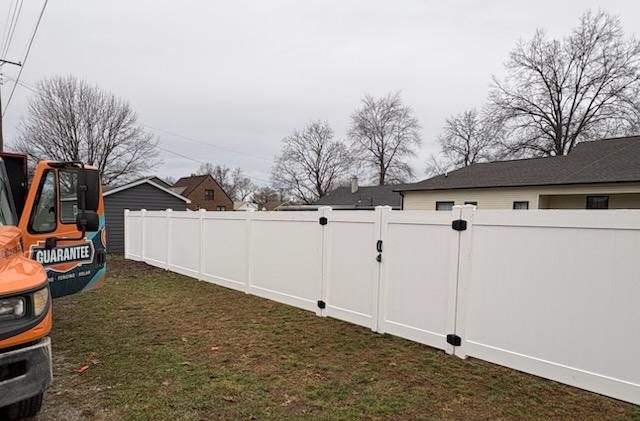 Image of Guarantee Roofing and Fence's orange and blue truck parked next to a newly installed, white vinyl fence.