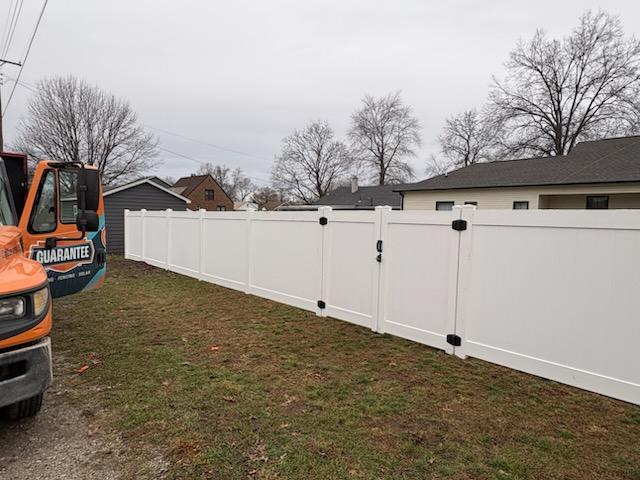 Image of Guarantee Roofing and Fence's orange and blue truck parked next to a newly installed, white vinyl fence.