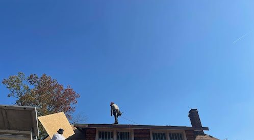 Total Roof Replacement being done by Guarantee Roofing and Fence. The wooden boards are being brought up in a lift. Two men are laying them and nailing them in place.