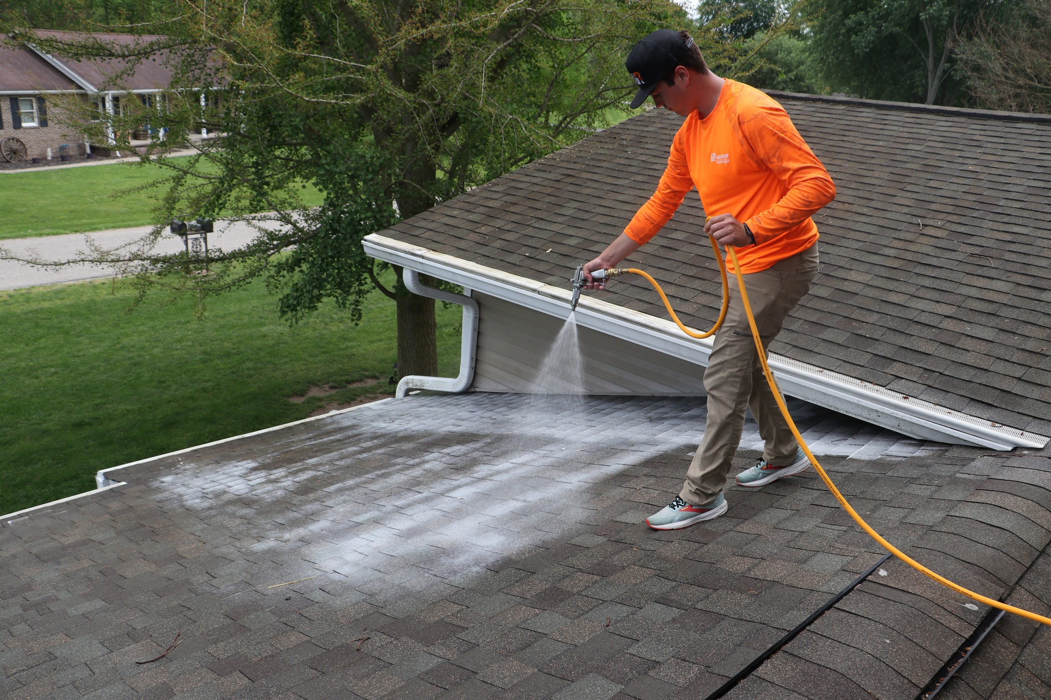 Roof Rejuvenation from Guarantee Roofing and Fence. Man wearing an orange shirt is spraying dirty shingles with cleaner and protectant for extend the life of the shingles.