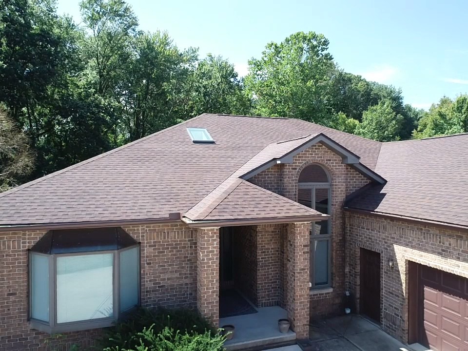 Aerial view of a brick home and its brown roof. There is a small skylight towards the top and a large window in the front.