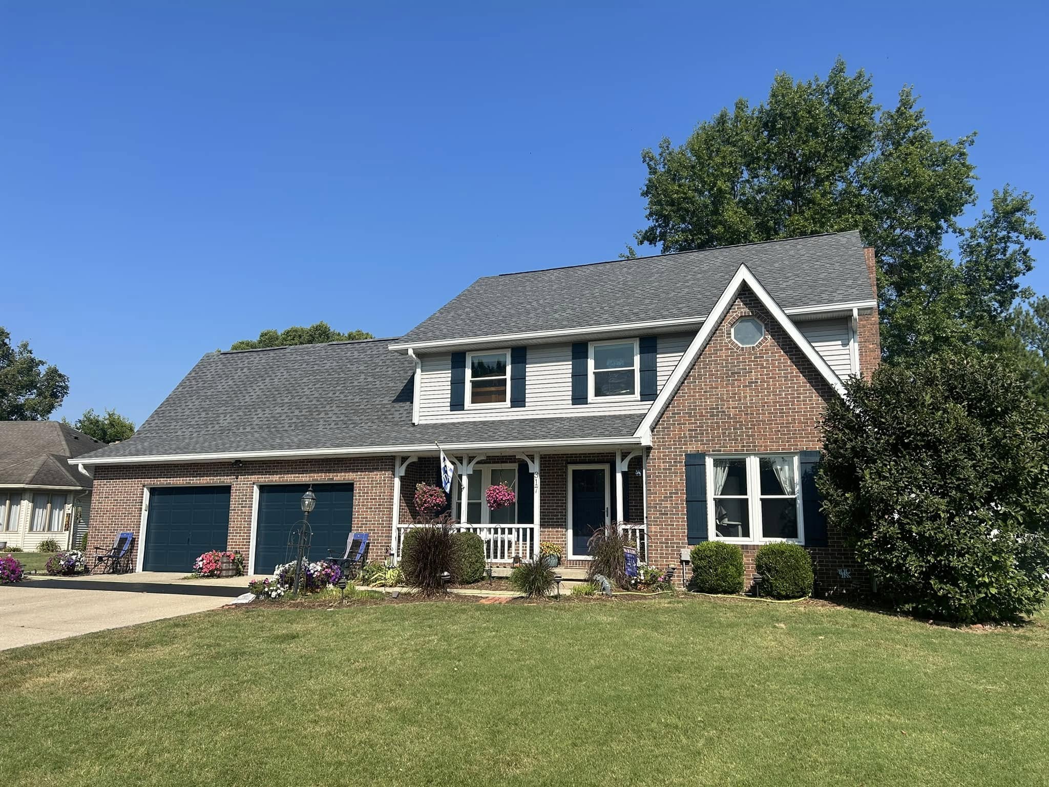 Two-story brick and siding home with a brand new roof from Guarantee Roofing and Fence. The garage and front door are a deep navy and the roof is a medium gray asphalt shingle.