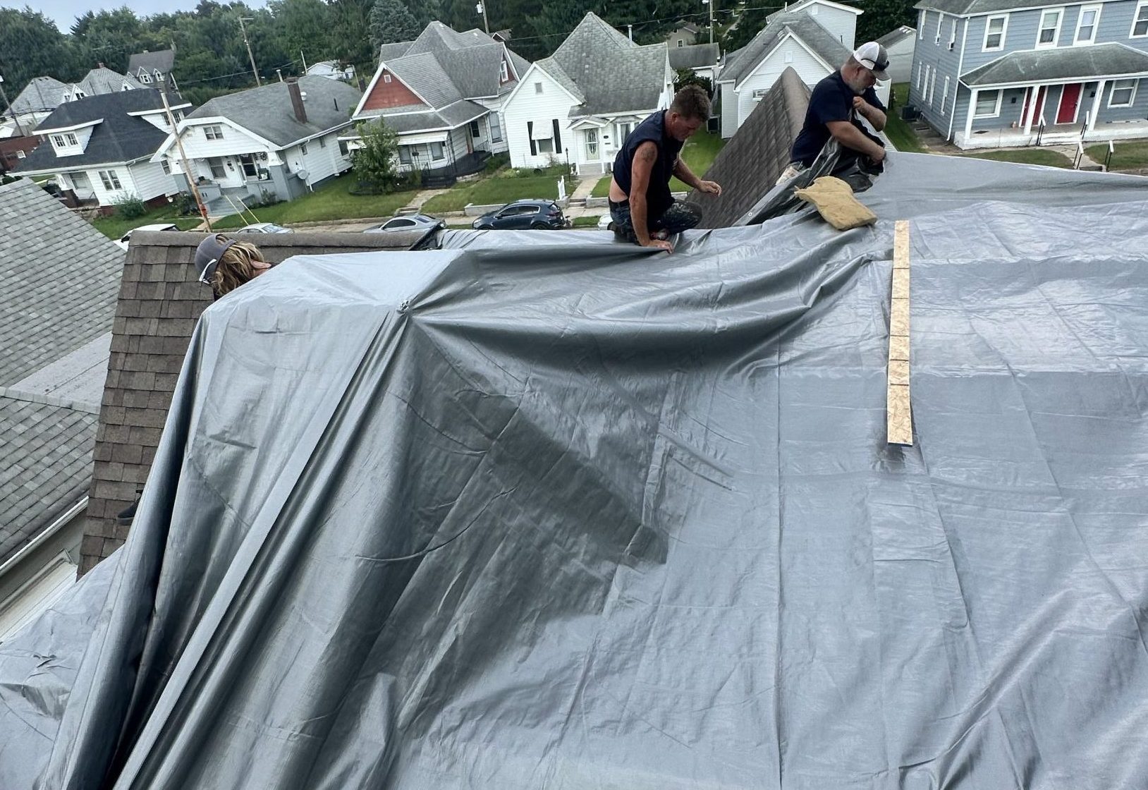 Guarantee Roofing and Fence adding a large, silver tarp to a homeowners roof as they had a major roof collapse after heavy rains. Guarantee offers emergency service to protect your home.
