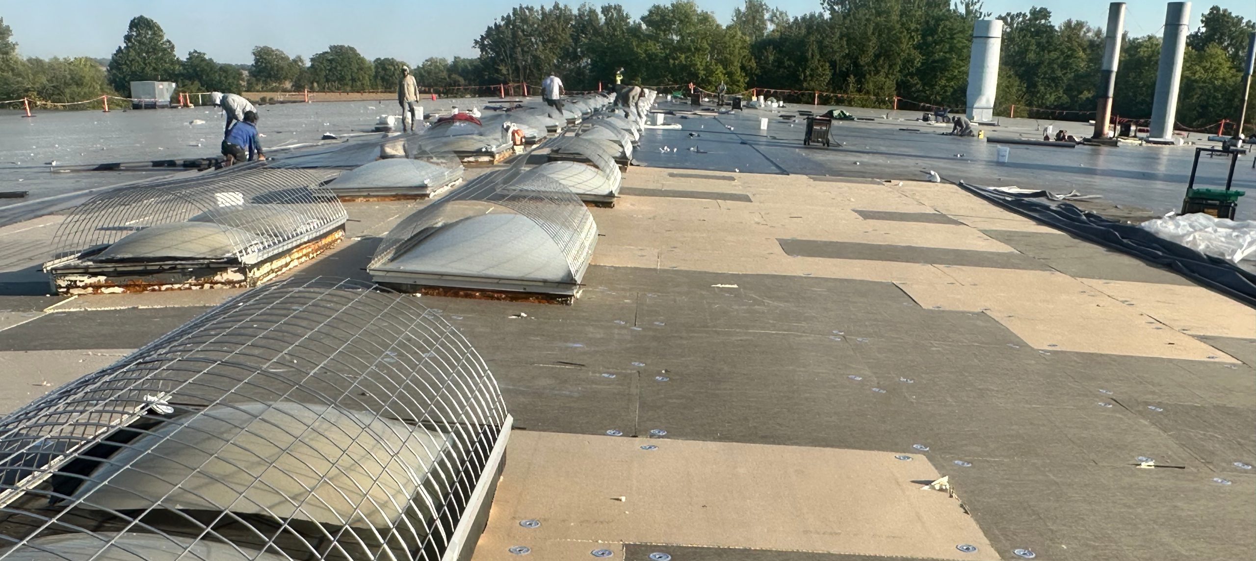 Commercial Roof replacement. The center is rows of metal wire protecting bubble skylights. Sections of the decking have been replaced and are a new, light tan color compared to the aged gray sections.